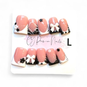 May include: A set of press-on nails with a pink base, white tips, and black accents. Some nails feature white bows, floral designs, and zebra stripes. The text "CY Press-on Nails" is visible.