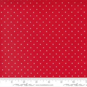 May include: Red fabric with a repeating pattern of small white stars. The fabric is measured with a ruler marked in inches. The fabric is from Moda Fabrics.