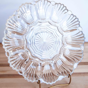 May include: Clear glass serving dish with a scalloped edge and multiple compartments. The dish has a starburst design in the center and is displayed on a gold-colored metal stand. The dish is designed for serving appetizers or snacks.