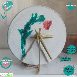 May include: Handcrafted concrete clock with green and red abstract art, gold hands, and a rope detail. The clock is 4.92 inches in diameter and weighs 0.66-0.75 lbs.