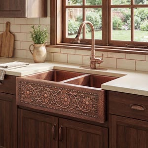 May include: A copper farmhouse sink with a floral design. The sink has two basins and is installed in a kitchen with dark wood cabinets and a copper faucet. The floral design is embossed on the front of the sink.