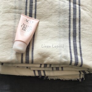 May include: A white linen fabric with blue stripes, folded in a stack. A tube of hand cream labeled "ACO Hand Cream Rich" is on top of the fabric.