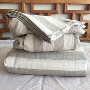 May include: A stack of three grey and white striped linen bedding pieces. The top piece is folded and has a button closure.