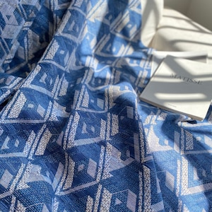 May include: A blue and white patterned throw blanket with a geometric design. The blanket is folded and draped over a white couch with a book titled "Matisse" on top.