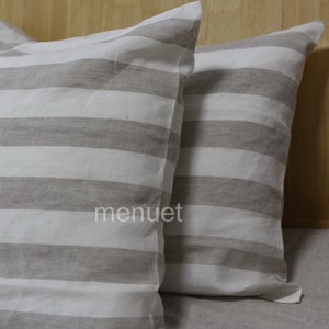 May include: Two striped pillowcases in a light grey and white colour scheme. The pillowcases are made of a soft, linen fabric.