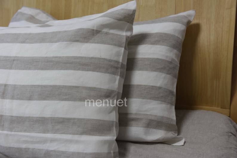 May include: Two striped pillowcases in a light grey and white colour scheme. The pillowcases are made of a soft, linen fabric.