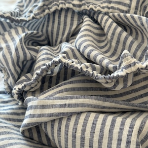 May include: Close-up of a blue and white striped fabric with a gathered edge. The fabric is made of a linen blend and has a soft, textured feel.