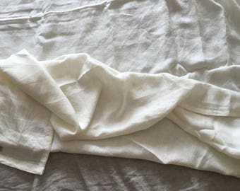 May include: A white linen fabric with a soft, crinkled texture. The fabric is folded and draped, creating a smooth, flowing look.