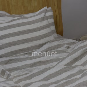 May include: A white and grey striped linen bedding set with a pillow and duvet cover. The bedding is made from natural linen and has a relaxed, casual look.