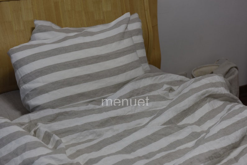 May include: A white and grey striped linen bedding set with a pillow and duvet cover. The bedding is made from natural linen and has a relaxed, casual look.