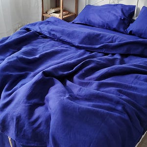 Op de afbeelding: Een bed is bedekt met een diepblauwe linnen beddengoedset. De set bevat een dekbedovertrek en twee kussenslopen. Het bed is opgemaakt met een hoeslaken en een bedrok. Het beddengoed is netjes opgemaakt.