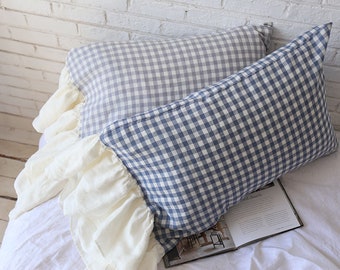 May include: Two pillowcases with ruffled edges. The pillowcases are made of a light blue and white gingham fabric. The pillowcases are stacked on top of each other.