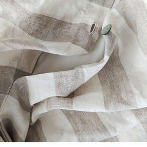 May include: Close-up of a white and brown striped fabric with a single button sewn on. The fabric is folded and creased, creating a textured look.