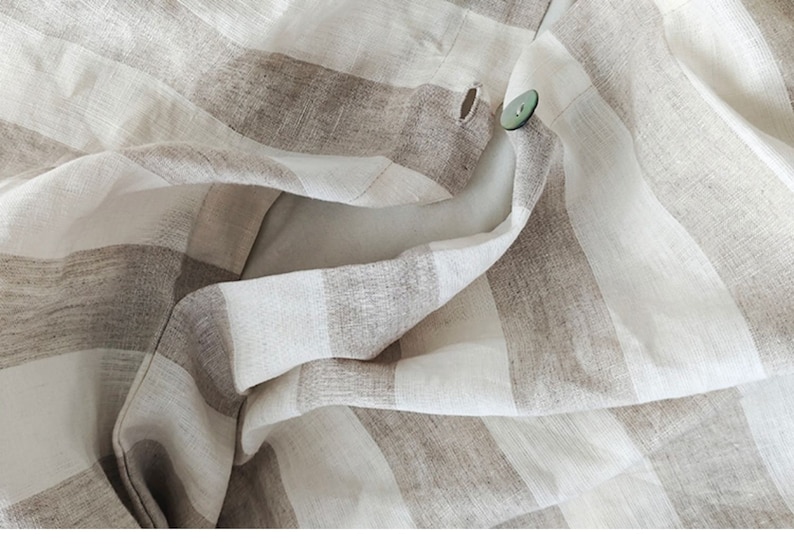 May include: Close-up of a white and brown striped fabric with a single button sewn on. The fabric is folded and creased, creating a textured look.