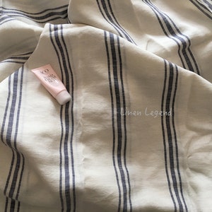 May include: A white linen fabric with blue stripes. The fabric is folded and a small tube of hand cream is on top of the fabric. The text on the tube reads "ACO Hand Cream Daily". The text "Linen Legend" is printed on the fabric.