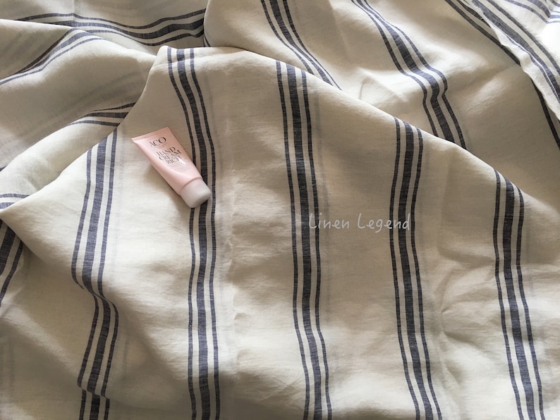 May include: A white linen fabric with blue stripes. The fabric is folded and a small tube of hand cream is on top of the fabric. The text on the tube reads "ACO Hand Cream Daily". The text "Linen Legend" is printed on the fabric.