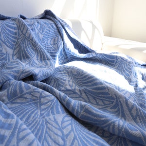 Puede incluir: Una manta de tiro azul con un patrón de hojas blancas. La manta está hecha de una tela suave y texturizada y es perfecta para agregar un toque de calidez y estilo a cualquier habitación.