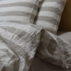 May include: A close-up of a white and grey striped linen bedding set. The bedding is made of soft, natural linen and has a relaxed, casual look.