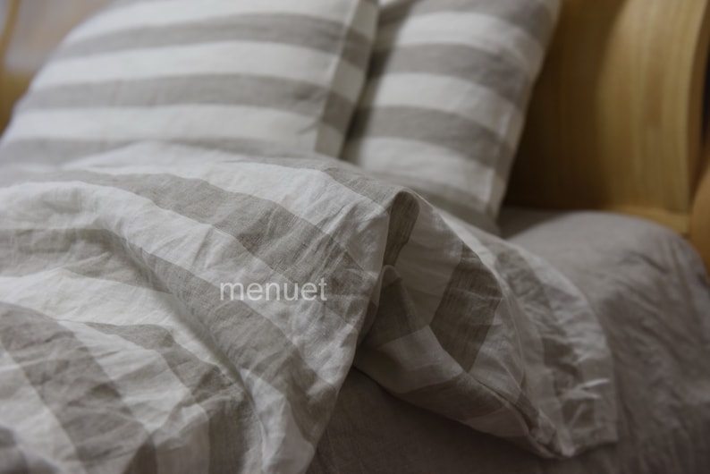 May include: A close-up of a white and grey striped linen bedding set. The bedding is made of soft, natural linen and has a relaxed, casual look.