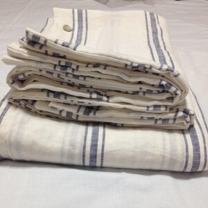 May include: A white and blue striped linen bedding set folded on a white surface.