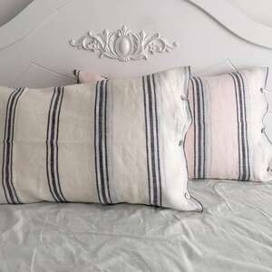 May include: Two white and blue striped pillowcases with a pink and white striped pillowcase on a white bed frame.