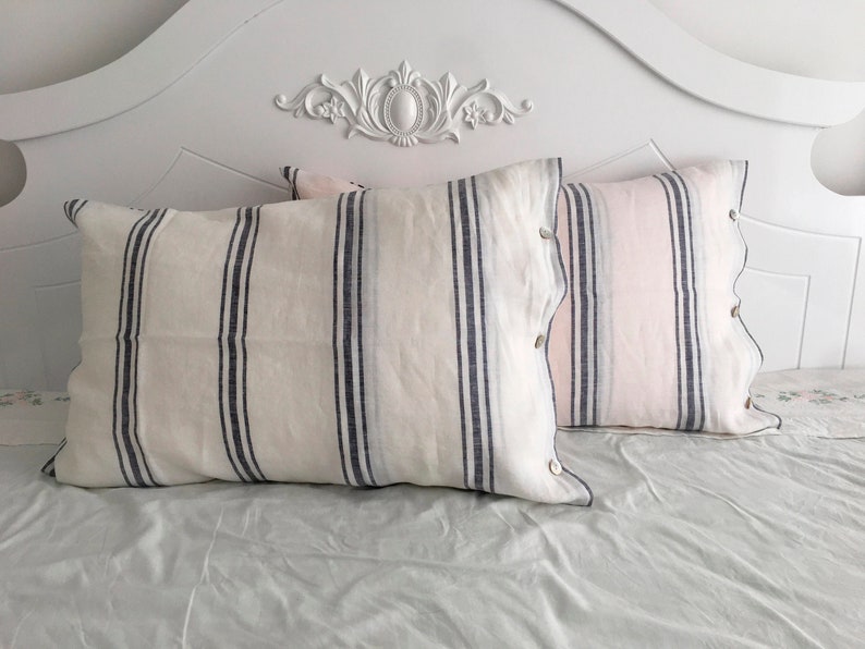 May include: Two white and blue striped pillowcases with a pink and white striped pillowcase on a white bed frame.