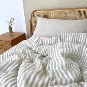 May include: A white and gray striped linen duvet cover on a bed with a woven headboard. The duvet cover is made of natural linen and has a relaxed, casual look.