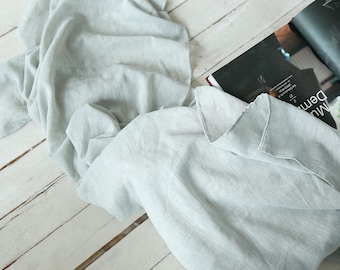 May include: A light gray linen fabric draped over a wooden surface. The fabric is soft and textured, with a subtle sheen.