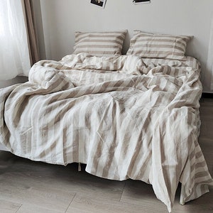 May include: A white and beige striped linen bedding set with a duvet cover, two pillowcases, and a flat sheet.