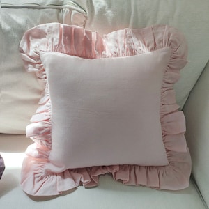 May include: A pink pillow with a ruffled border. The pillow is made of a soft, light fabric and has a square shape.