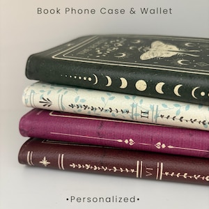 May include: A stack of four rectangular book-style phone case wallets. The top case is dark green with gold moon phases. The second is cream with blue leaves. The third is deep purple with gold lines. The bottom is dark brown with gold floral details.