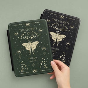 May include: Two e-reader covers, one dark green and one black, with a celestial design. The covers feature a moth illustration, the text "THE SECRETS OF", and the author's name, "MATILDA SMITH". The covers are on a light green background.