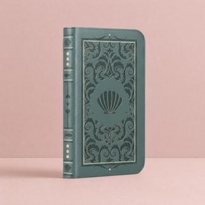 May include: A teal-colored book cover with a seashell design. The cover features an embossed seashell in the center, surrounded by ornate scrollwork. The spine has decorative elements, including small dots and fish symbols. The book is standing upright.