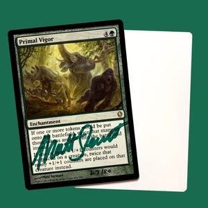 May include: A green Magic: The Gathering card with the title "Primal Vigor" and the text "If one or more tokens would be put onto the battlefield, twice that many of those tokens are put onto the battlefield instead. If one or more +1/+1 counters would be placed on a creature, twice that many +1/+1 counters are placed on that creature instead." The card is signed by Matt Stewart and numbered 27/50.