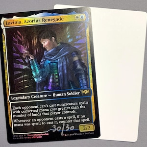 May include: A Magic: The Gathering card featuring Lavinia, Azorius Renegade, a legendary creature with a blue and white colour scheme. The card has a foil finish and is signed by Matt Stewart. The card text reads: "Each opponent can't cast noncreature spells with converted mana cost greater than the number of lands that player controls. Whenever an opponent casts a spell, if no mana was spent to cast it, counter that spell."
