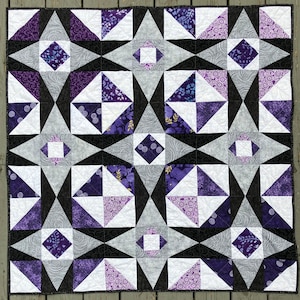 Könnte beinhalten: Eine Steppdecke mit einem geometrischen Muster aus schwarzen, weißen und violetten Dreiecken. Die Steppdecke besteht aus vielen kleineren Quadraten, die jeweils ein anderes Muster haben.