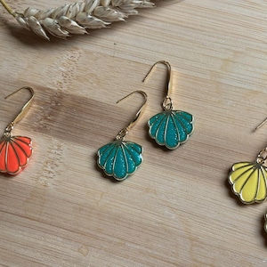 Peut inclure: Trois paires de boucles d'oreilles pendantes avec des crochets en métal doré et des breloques en forme de coquillage. Une paire est orange vif, une paire est bleu sarcelle et une paire est jaune pâle. Finition émaillée lisse et bords dorés.