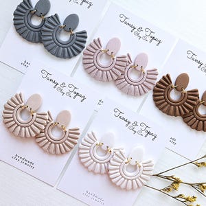 May include: Four pairs of handmade clay earrings in various colors, including gray, pink, white, and brown. Each pair features a fan-shaped design with a hoop-style earring.