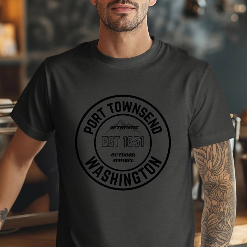 A man in a coffee shop wears a dark grey heather aqua bella canvas 3001 with a circle graphic reading port townsend washington authentic outdoor apparel.