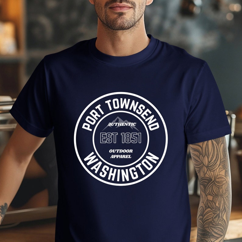 A man in a coffee shop wears a navy bella canvas 3001 with a circle graphic reading port townsend washington authentic outdoor apparel.