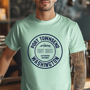 A man in a coffee shop wears a heather mint aqua bella canvas 3001 with a circle graphic reading port townsend washington authentic outdoor apparel.