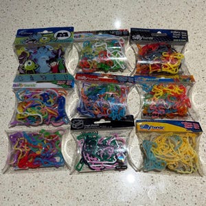 May include: A selection of Silly Bandz, colourful rubber band shapes, in clear plastic packaging. Some packs feature Disney's Monsters, Inc. characters and NHL logos. Each pack is labelled with the Silly Bandz brand.