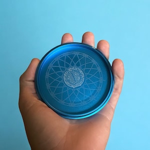 Puede incluir: Un molinillo de metal azul con un diseño circular y un patrón de mandala blanco.