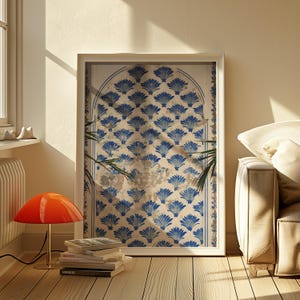 Puede incluir: Una impresión enmarcada de un arco de azulejos azules y blancos con un patrón decorativo de hojas estilizadas. El arco está situado contra una pared blanca y está enmarcado en un marco blanco.