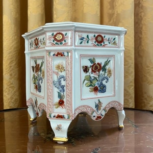May include: White porcelain hexagonal planter with gold accents and floral designs in red, blue, and yellow. The planter has three legs and a scalloped edge.