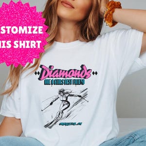 May include: White t-shirt featuring a graphic of a woman skiing and the text "Diamonds are a girls best friend".