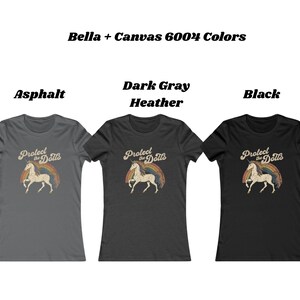 May include: Three Bella + Canvas 6004 t-shirts in Asphalt, Dark Gray Heather, and Black. Each shirt features a vintage-style graphic of a unicorn with a rainbow and the text "Protect the Dolls".