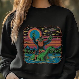 Bigfoot Riding Dinosaur T-Shirt - Funny Sasquatch Cowboy Graphic Tee - Retro Cryptid Adventure Shirt - Unique Gift for Bigfoot Lovers