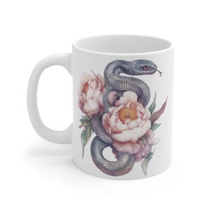 Op de afbeelding: Een witte keramische mok met een grijze slang die om roze pioenen is gewikkeld. De slang heeft een zwart oog en een witte achtergrond.