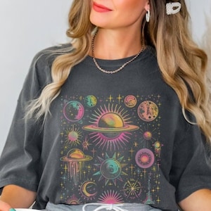 May include: A dark grey t-shirt featuring a colourful graphic print of planets, stars and moons. The graphic has a retro style with a faded, vintage look.